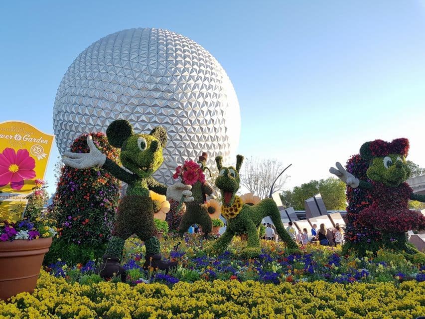 Des topiaires de Mickey Mouse, Pluto et Minnie Mouse se dressent dans un parterre de fleurs éclatant, avec une grande sphère géodésique en arrière-plan.