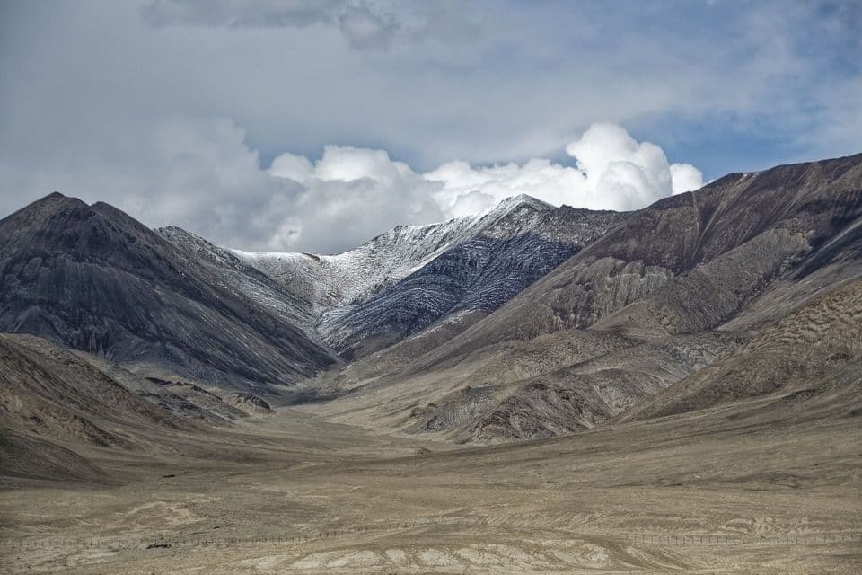 Montagne aspre e brulle con cime innevate si ergono sopra un'ampia valle arida sotto un cielo nuvoloso.