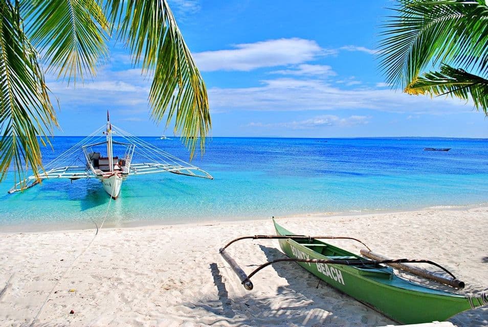 Dos canoas tradicionales en una playa de arena blanca y aguas turquesas, enmarcadas por palmeras bajo un cielo azul.