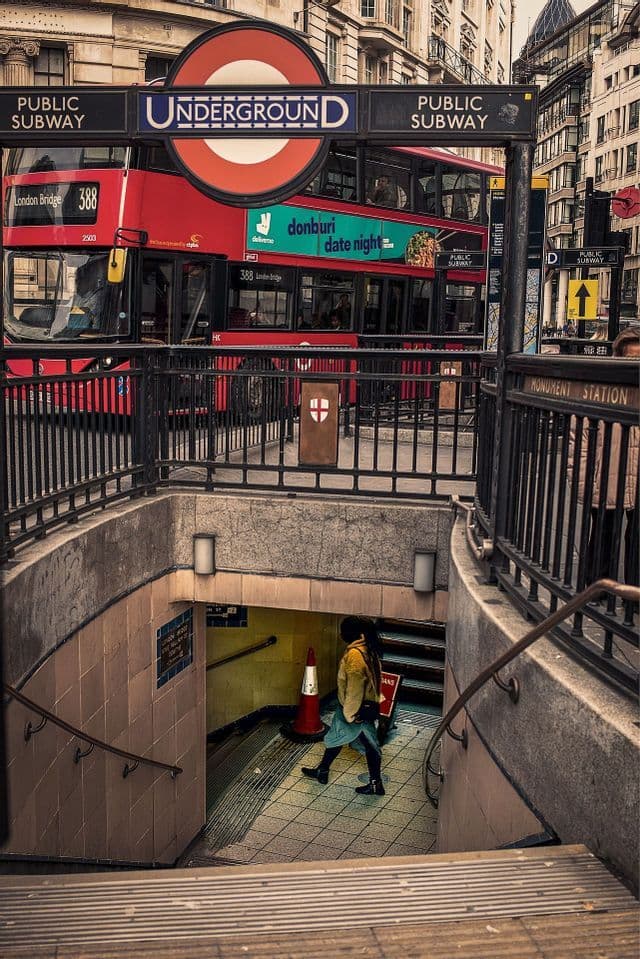 Una persona scende le scale verso l'ingresso di una stazione della metropolitana di Londra mentre un autobus rosso a due piani passa sulla strada.