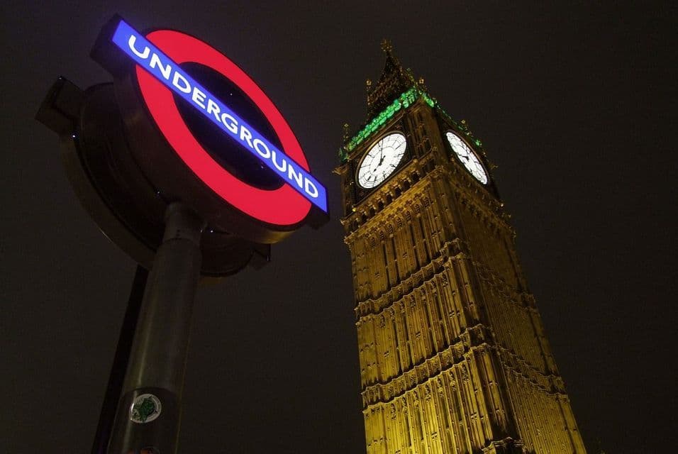 L'insegna illuminata della metropolitana di Londra e la torre dell'orologio del Big Ben visti da un'angolazione bassa di notte.