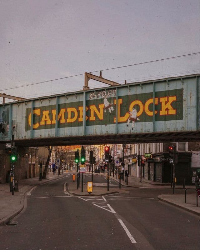 Il ponte ferroviario di Camden Lock si estende su una tranquilla strada urbana con semafori sotto un cielo velato.