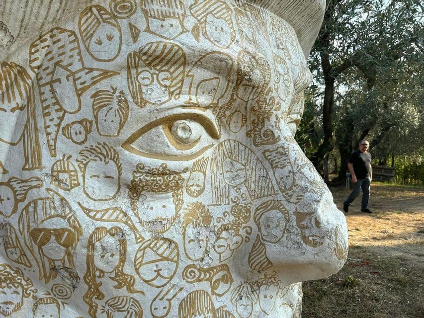 Un profilo ravvicinato di una grande scultura di testa bianca, la cui superficie è decorata con numerosi disegni a linee d'oro di volti a fumetto.
