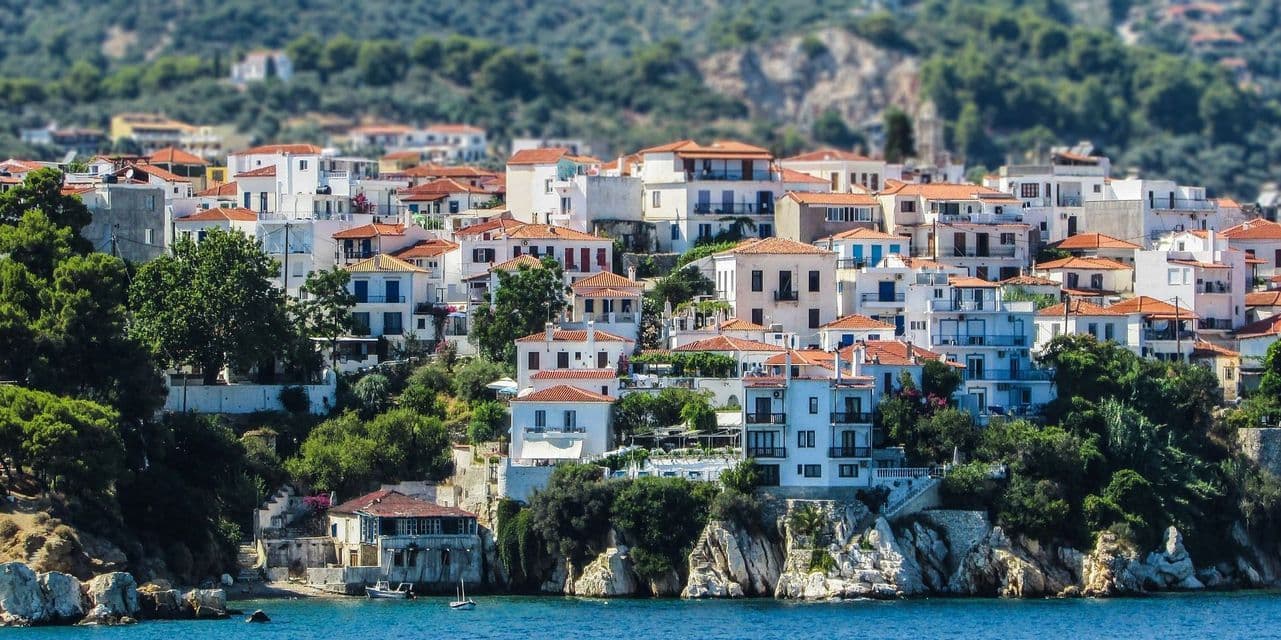 Un denso gruppo di edifici bianchi con tetti in terracotta costruiti su una lussureggiante collina verde che si affaccia su un mare blu calmo.