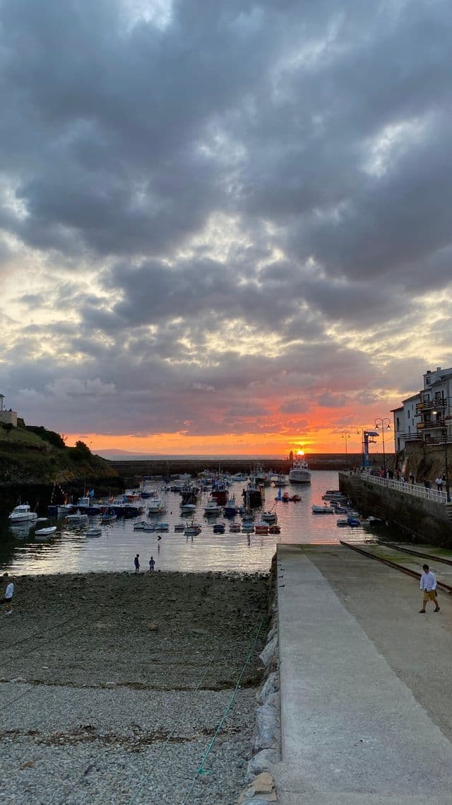 Un porto pieno di piccole barche che galleggiano sull'acqua al tramonto, sotto un cielo nuvoloso.