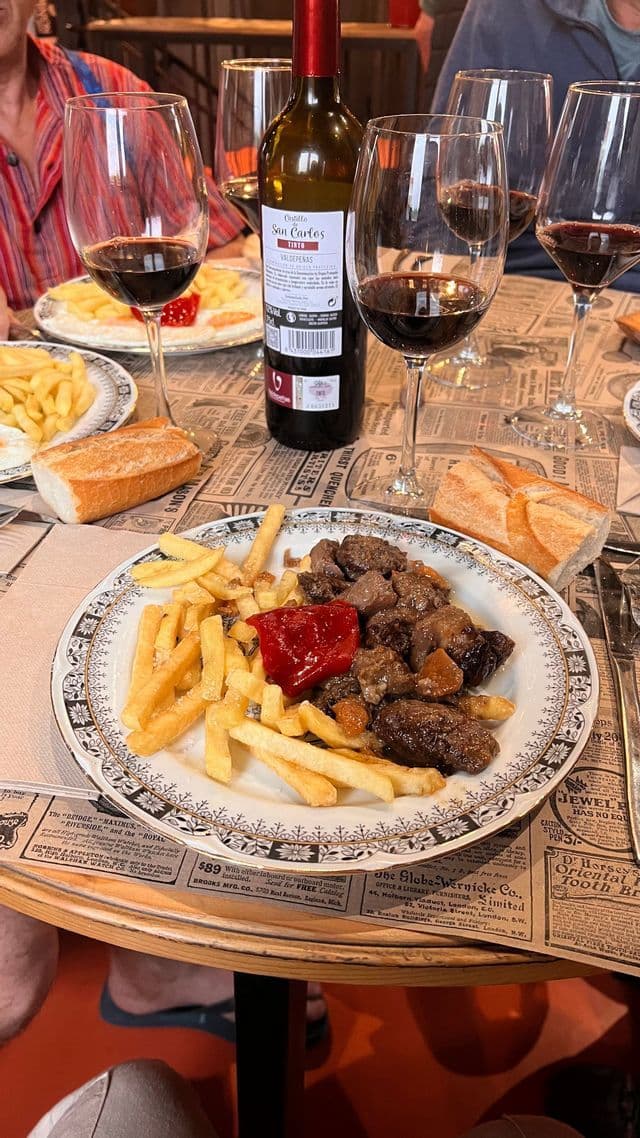 Un tavolo apparecchiato per un viaggio di gruppo WeRoad con un piatto di spezzatino di carne, patatine fritte, pane, una bottiglia e bicchieri di vino rosso.