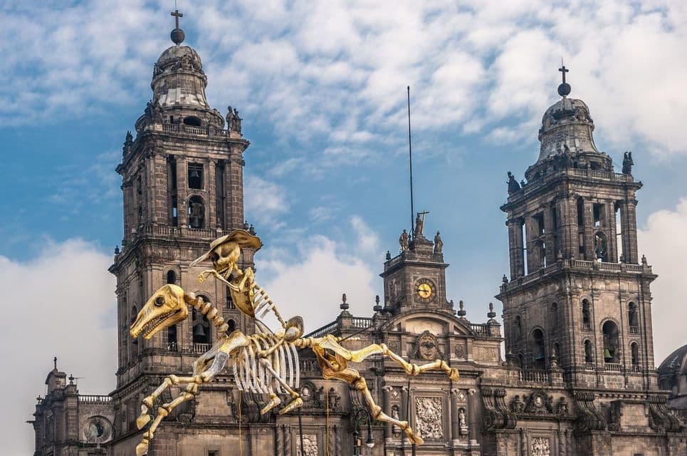 Un gran títere de esqueleto con sombrero monta un caballo esqueleto frente a una antigua catedral de piedra.
