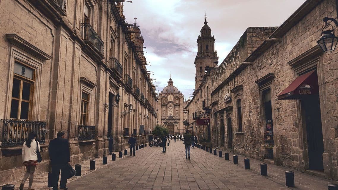 Vista de una calle empedrada flanqueada por edificios históricos, que conduce a una gran catedral con cúpula bajo un cielo nublado.