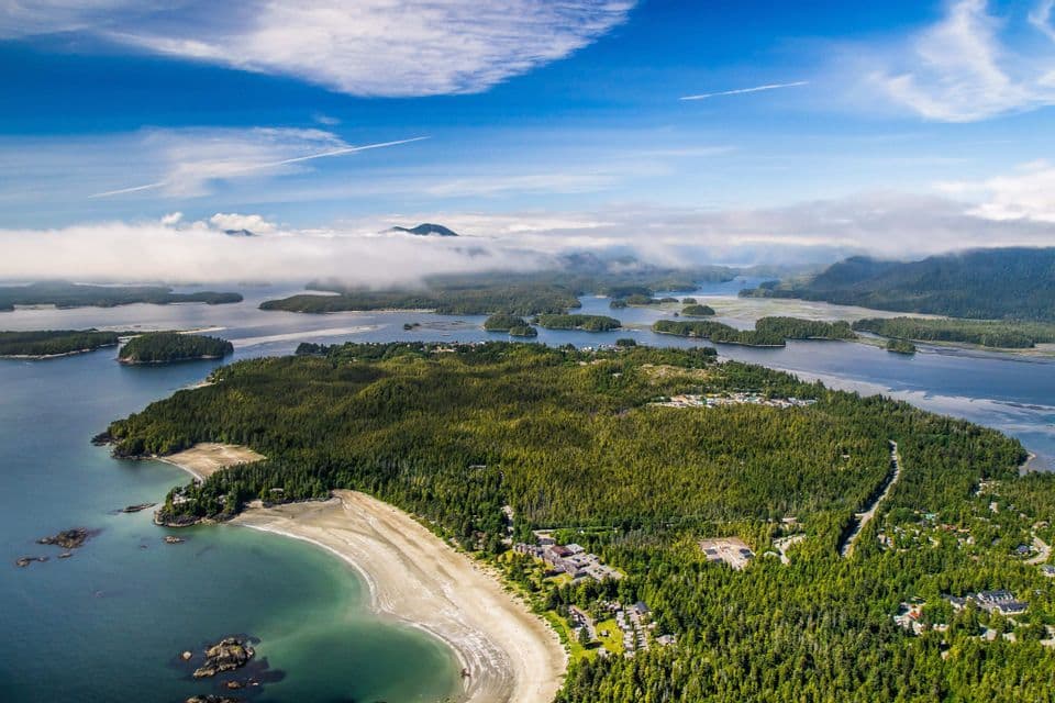 Vue aérienne d'un archipel boisé avec une plage de sable en forme de croissant, des îles éparses et des nuages bas