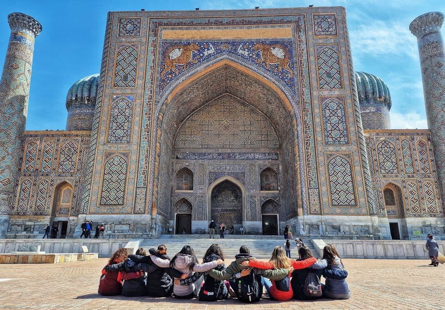 A WeRoad group trip sits with their backs to the camera, arms linked, admiring a grand, ornate building with intricate mosaic tilework.