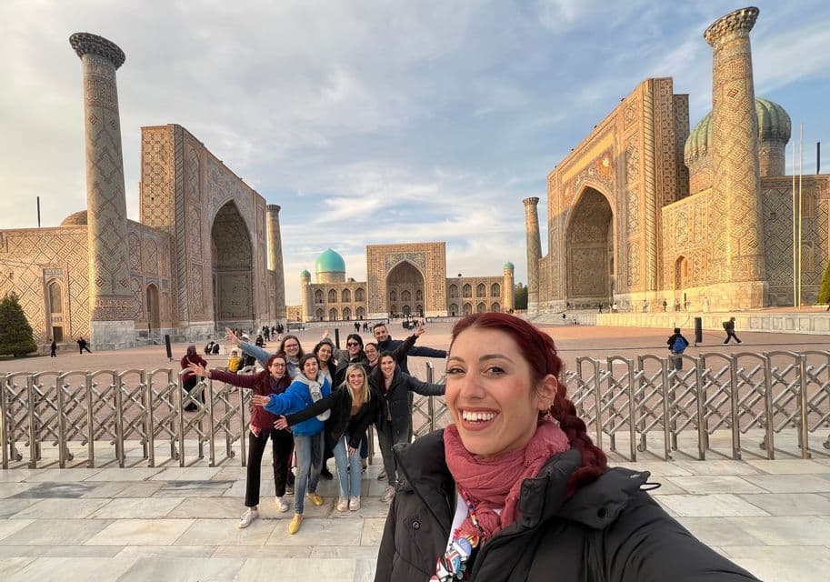 A woman takes a selfie with a WeRoad group trip posing in a large square in front of ornate historical buildings.