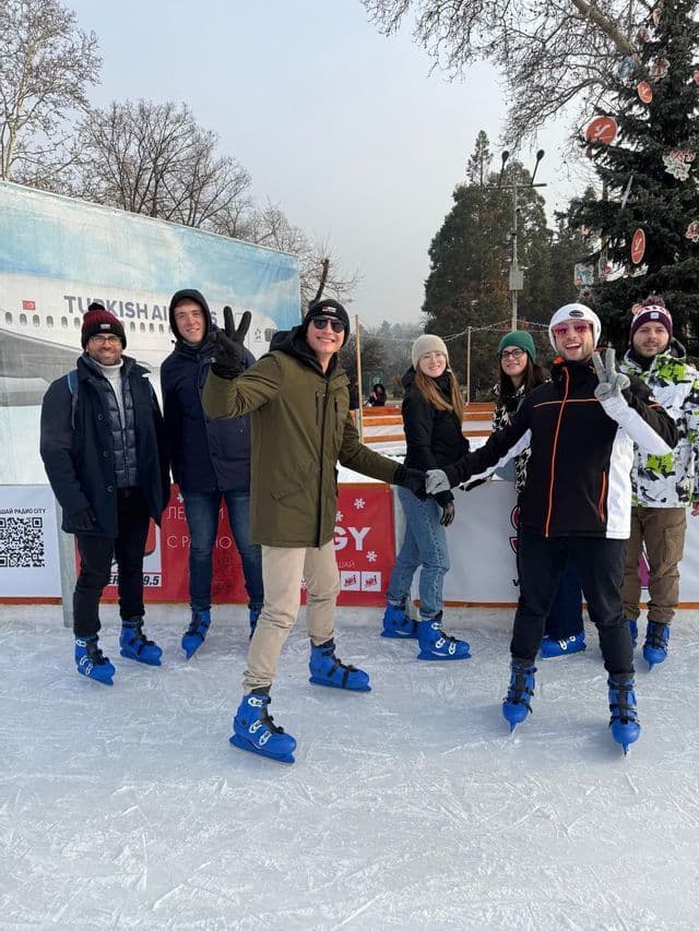 Un gruppo WeRoad in viaggio posa su una pista di pattinaggio all'aperto, con indosso abbigliamento invernale e pattini da ghiaccio blu.