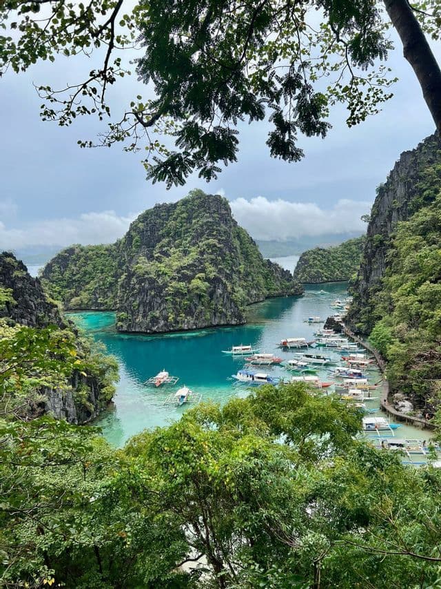 Veduta aerea di una laguna tropicale con acqua turchese e molte barche ormeggiate vicino a scogliere verdi e rocciose.