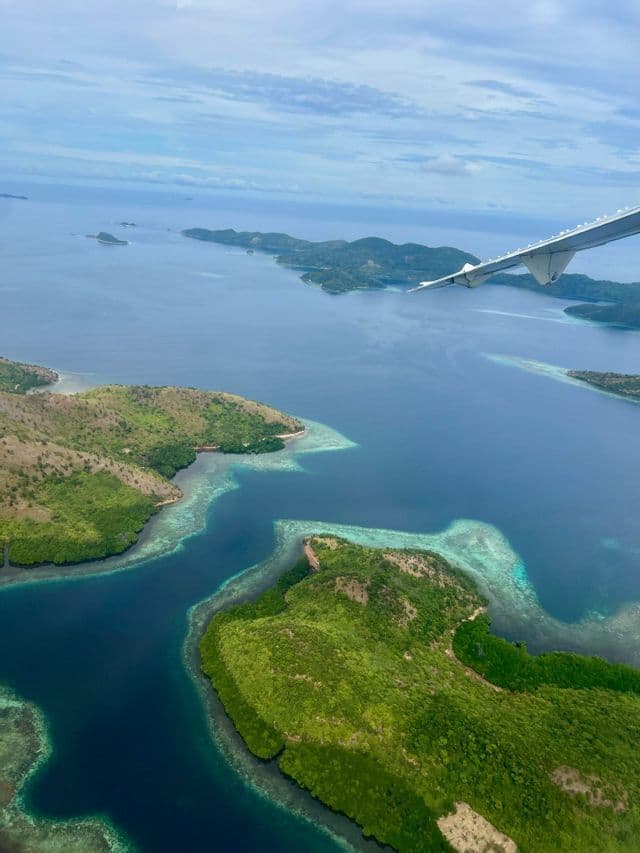 Vista aerea da un aereo su un arcipelago tropicale di isole verdi circondate da mare blu e barriere coralline turchesi.