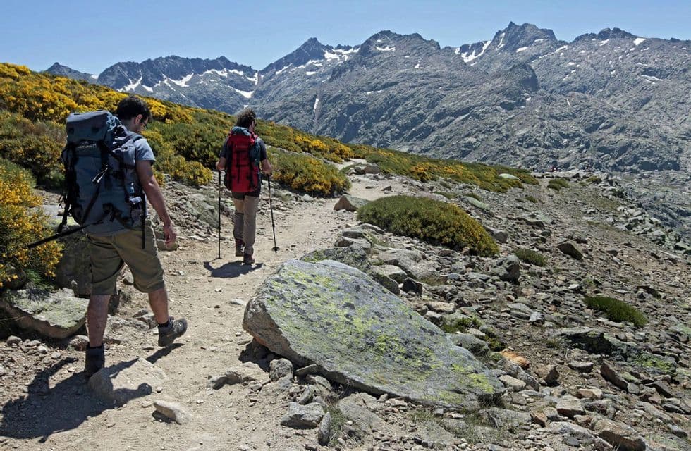 Un viaje en grupo de WeRoad de senderismo por un sendero a través de un paisaje rocoso con montañas nevadas al fondo.