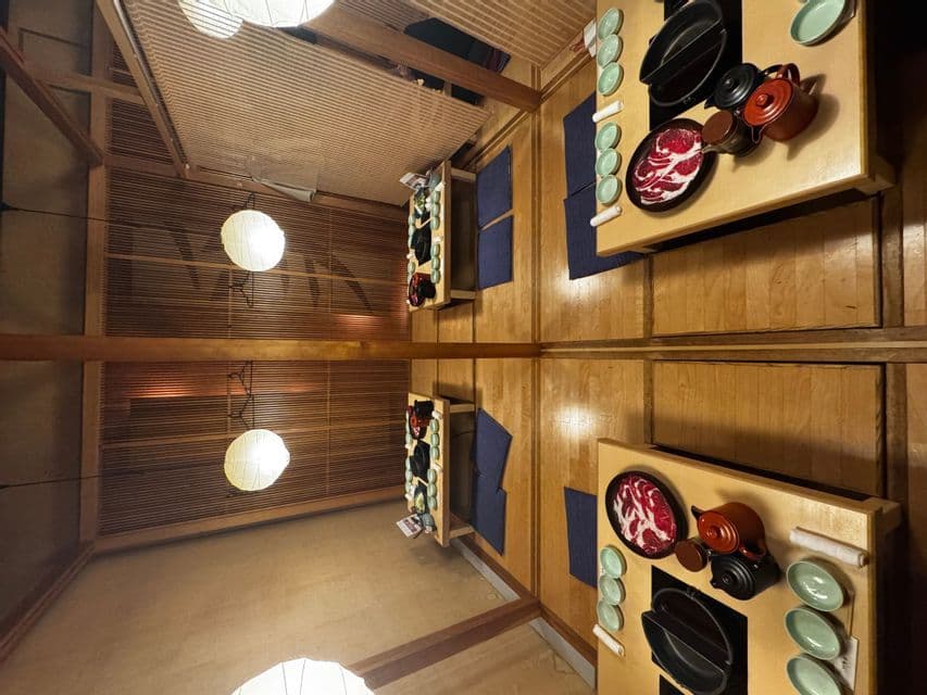 Tavoli apparecchiati per un pasto hot pot giapponese si riflettono perfettamente in un soffitto a specchio, creando una composizione completamente simmetrica.