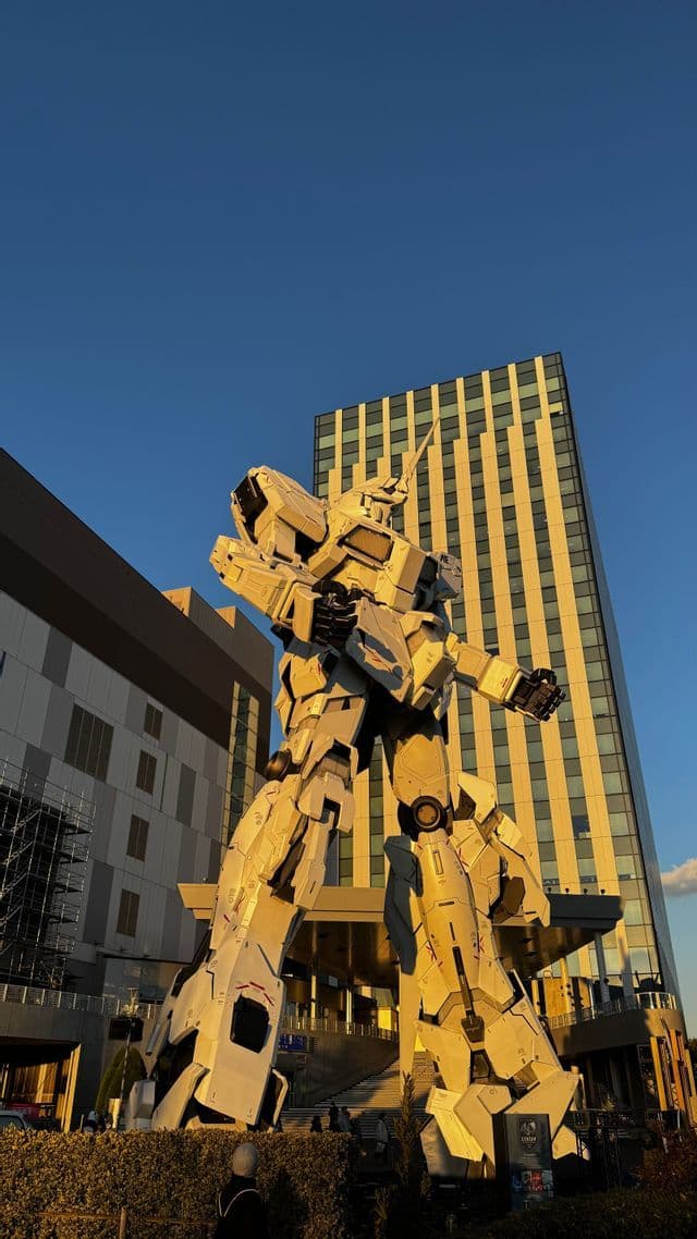Una statua gigante di robot bianco si erge in una piazza cittadina di fronte a un grattacielo, illuminata dalla luce dell'ora d'oro.