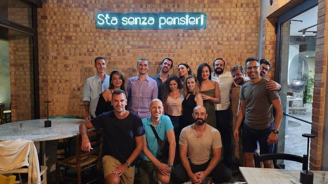 Un gruppo WeRoad sorride e posa per una foto davanti a un muro di mattoni con un'insegna al neon.