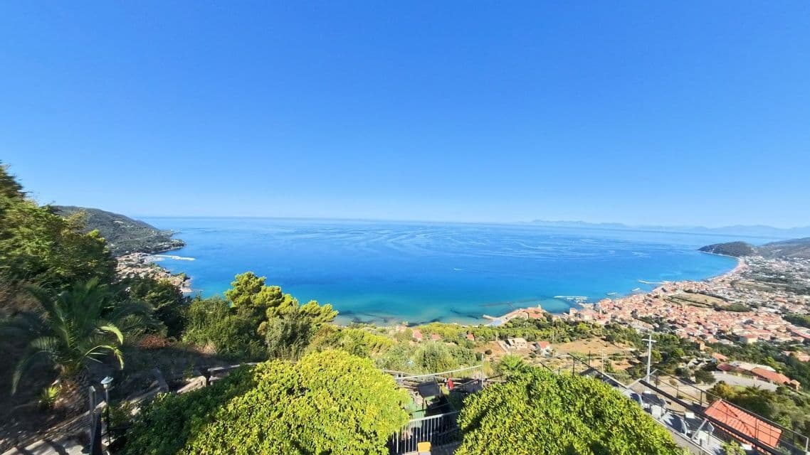 Una vista panoramica da un punto di osservazione elevato di una città costiera costruita lungo un'ampia baia con acqua blu sotto un cielo sereno.