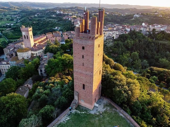 Una veduta aerea di una torre in mattoni rossi che domina una città storica immersa tra verdi colline ondulate al tramonto.