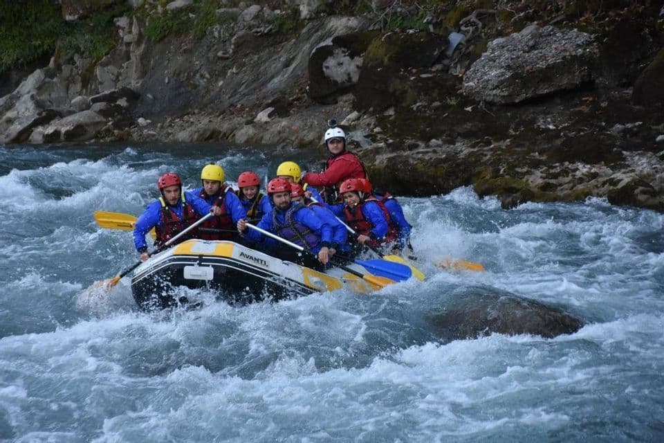 Un viaje en grupo de WeRoad navega por un río turbulento en una balsa inflable, remando a través de rápidos de aguas bravas.