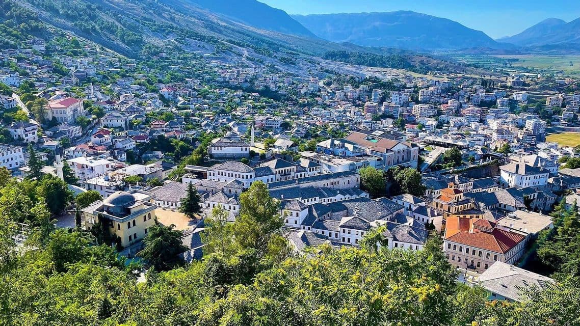 Una vista aérea de un pueblo histórico con edificios blancos y tejados de piedra, enclavado en un valle verde al pie de las montañas.