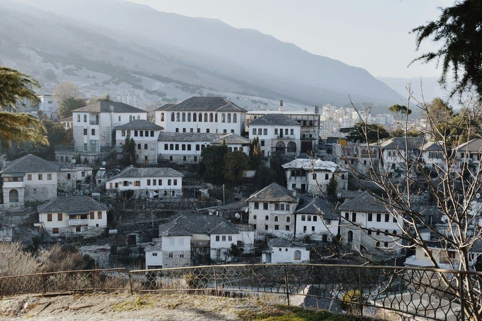 Casas de piedra blanca con techos oscuros construidas en una ladera con una gran cordillera nebulosa al fondo.