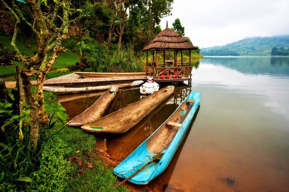 Canoas de madera amarradas en la orilla cubierta de hierba de un lago tranquilo con un cenador de techo de paja en un muelle.
