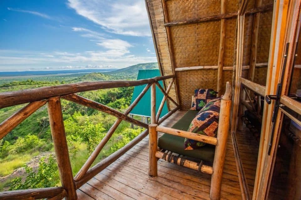 Un banco de madera en el balcón de una cabaña rústica, con vistas a un extenso paisaje de colinas verdes bajo un cielo parcialmente nublado.