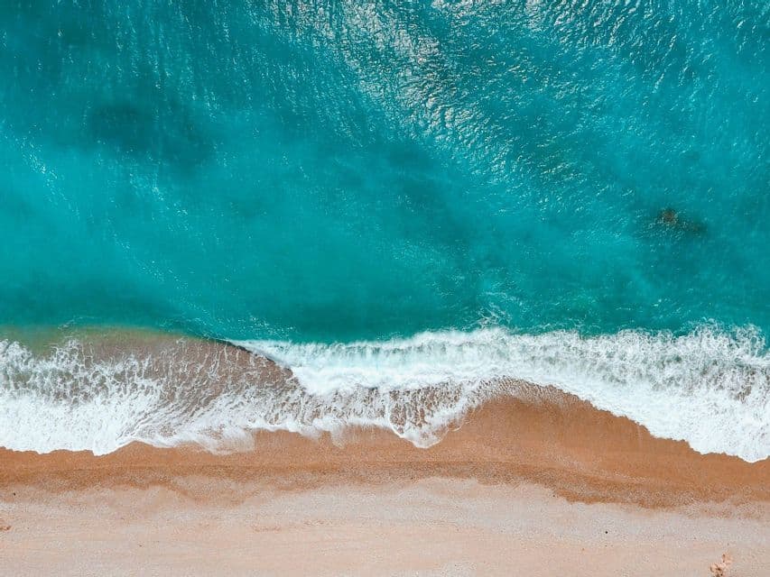 Una vista aérea cenital de olas turquesas con espuma blanca rompiendo en una playa de arena.