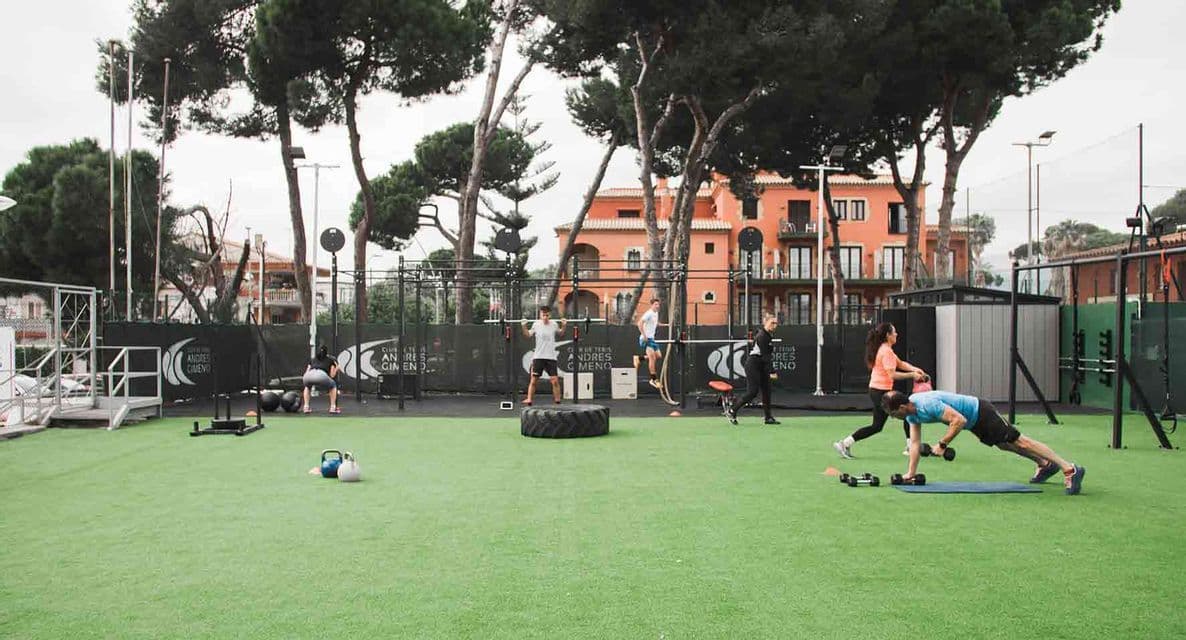 Un gruppo di persone che si allena con pesi e attrezzature in una palestra all'aperto su un campo in erba sintetica.