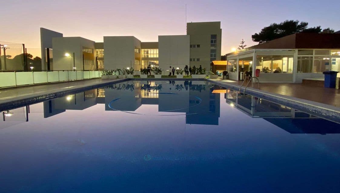 Una piscina che riflette un moderno edificio alberghiero al crepuscolo, con persone di un viaggio di gruppo WeRoad in piedi nelle vicinanze.