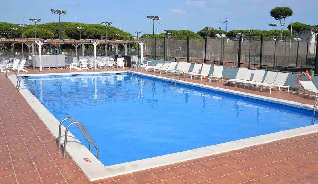 Una piscina esterna vuota con acqua azzurra, circondata da sdraio bianche su un solarium piastrellato in terracotta.