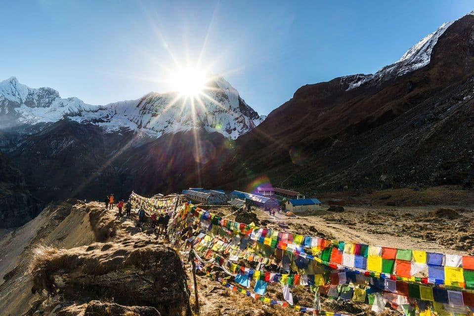 Un groupe WeRoad sur une crête de montagne avec des drapeaux de prière colorés, au lever du soleil sur des pics enneigés.
