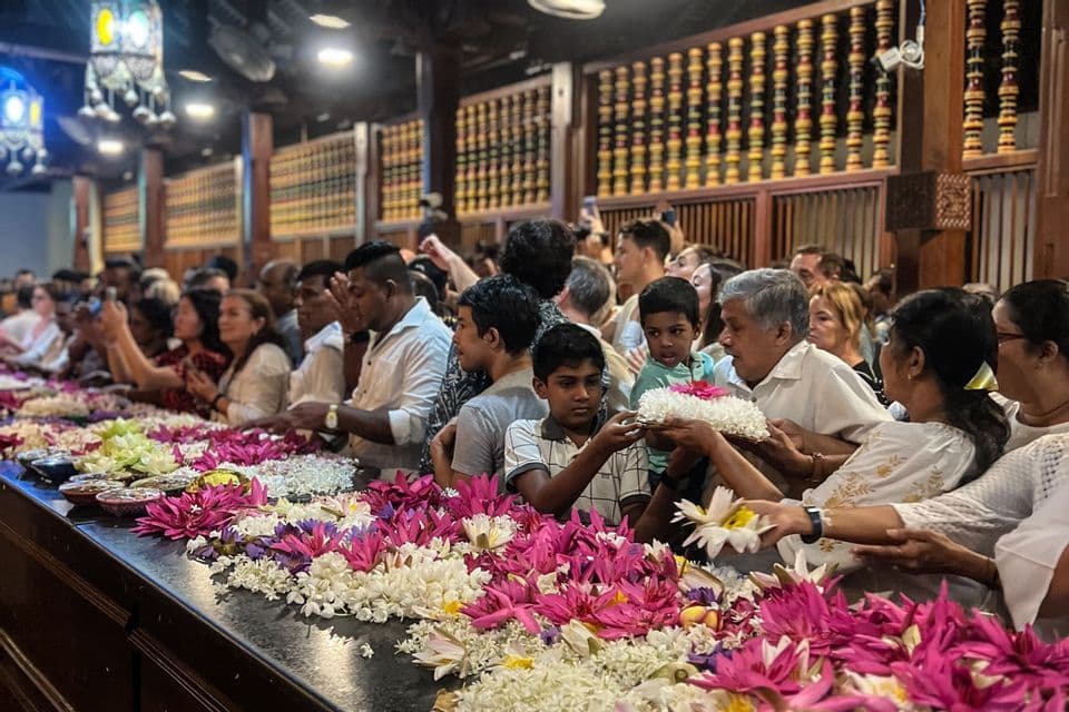 Una folla di persone che fanno offerte a un lungo altare coperto di ninfee rosa e bianche all'interno di un edificio ornato.