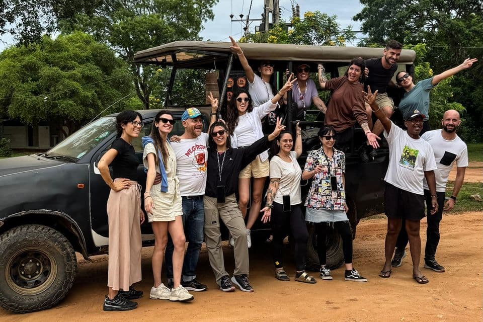 Un groupe WeRoad en voyage, souriant et posant pour une photo de groupe, à bord et autour d'une jeep de safari sur une piste de terre.