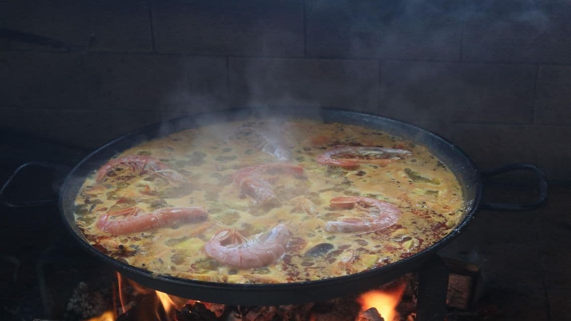 Una grande padella di paella ai frutti di mare con gamberi, fumante mentre cuoce su un fuoco a legna.