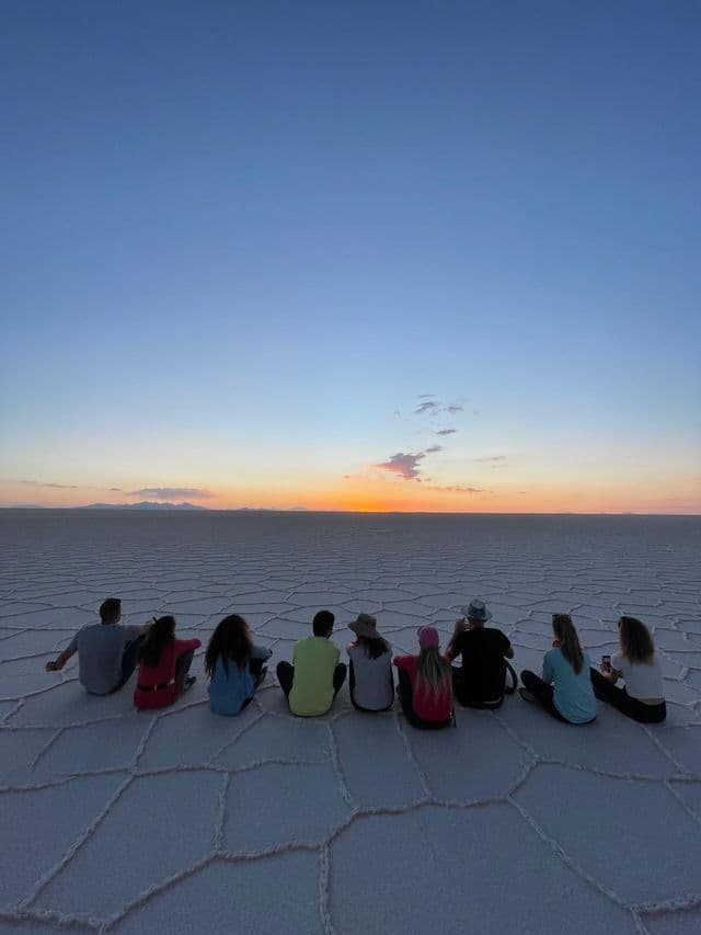 Un viaje en grupo de WeRoad visto desde atrás, sentados en un vasto salar viendo el atardecer en el horizonte.
