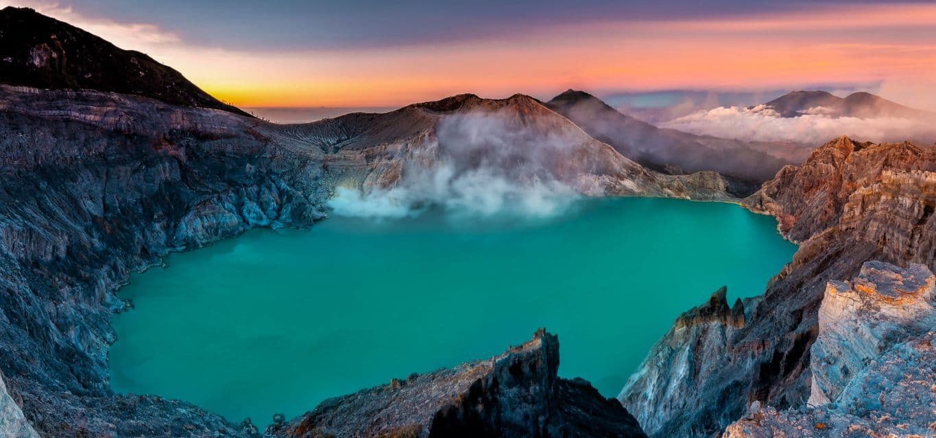 Vista panorámica de un vibrante lago turquesa en cráter volcánico, con vapor emergiendo de las laderas rocosas al amanecer.