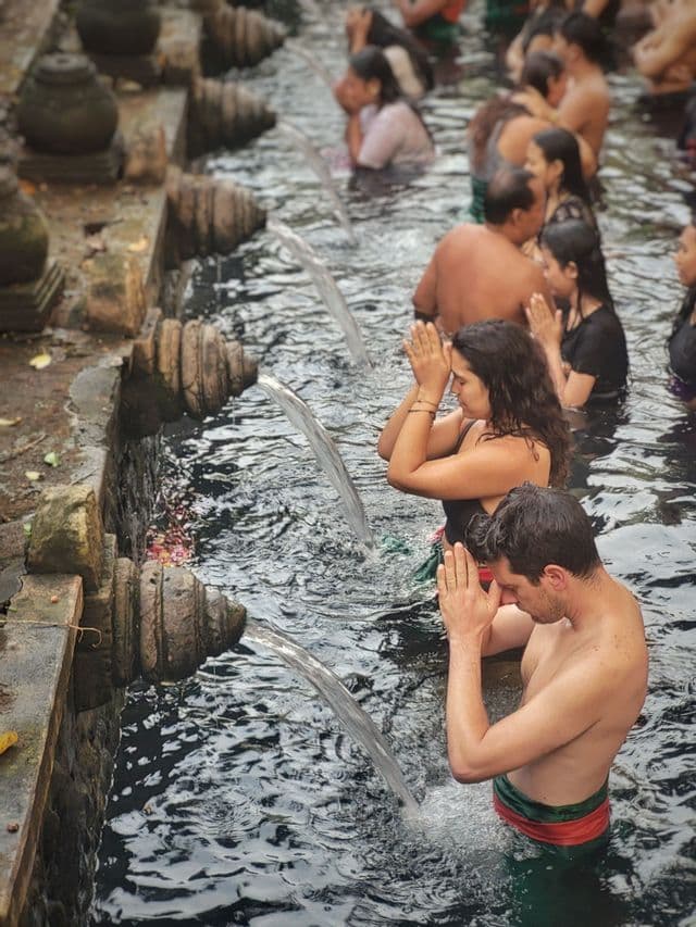Un grupo de WeRoad realiza un ritual de purificación de agua bajo una hilera de caños de piedra, con las manos en posición de oración.