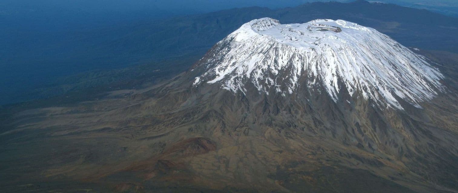 Vue aérienne d'un grand volcan endormi avec un sommet enneigé et un cratère s'élevant au-dessus d'un vaste paysage rocheux
