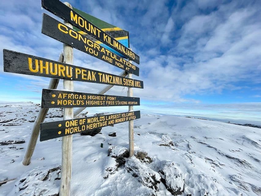 Le panneau en bois marquant le sommet du Pic Uhuru sur le Mont Kilimandjaro, se dressant dans un paysage enneigé sous un ciel partiellement nuageux.