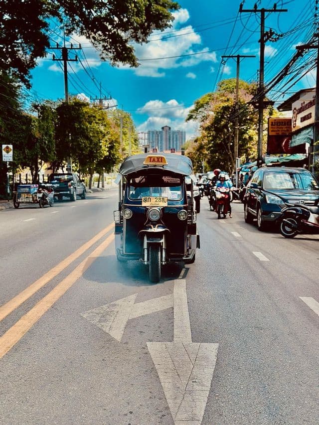Un taxi tuk-tuk circula por una calle arbolada, pasando sobre una gran flecha pintada en el asfalto.