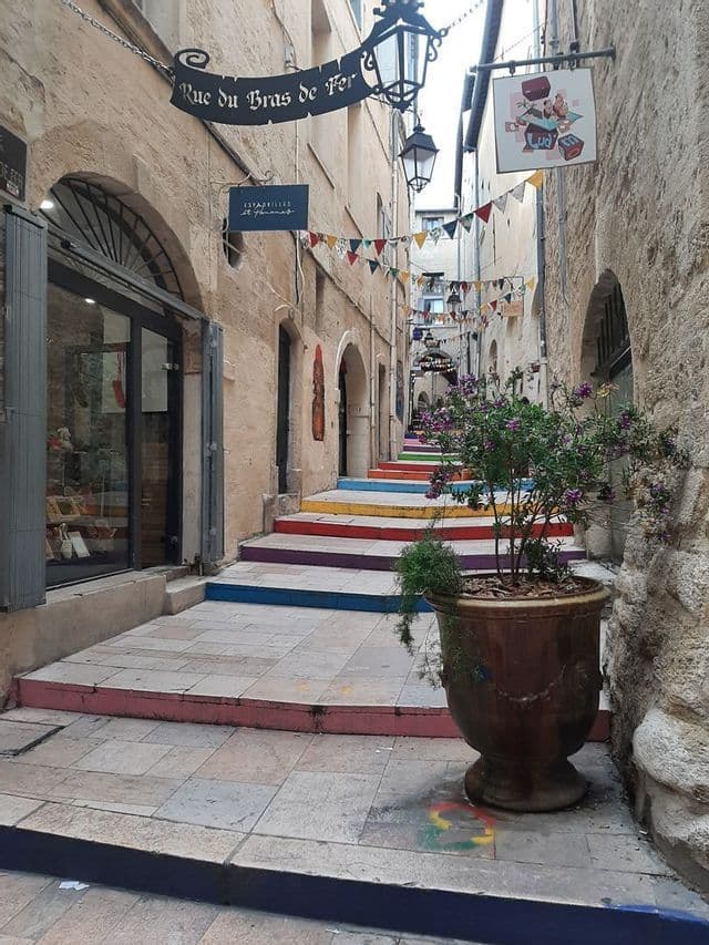 Une ruelle étroite en pierre avec un escalier peint aux couleurs de l'arc-en-ciel et des guirlandes colorées suspendues au-dessus.