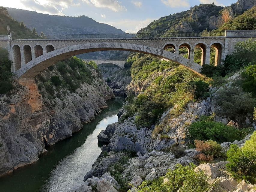 Deux ponts de pierre arqués enjambent une gorge profonde et rocheuse, traversée par une rivière, entourée de collines verdoyantes.