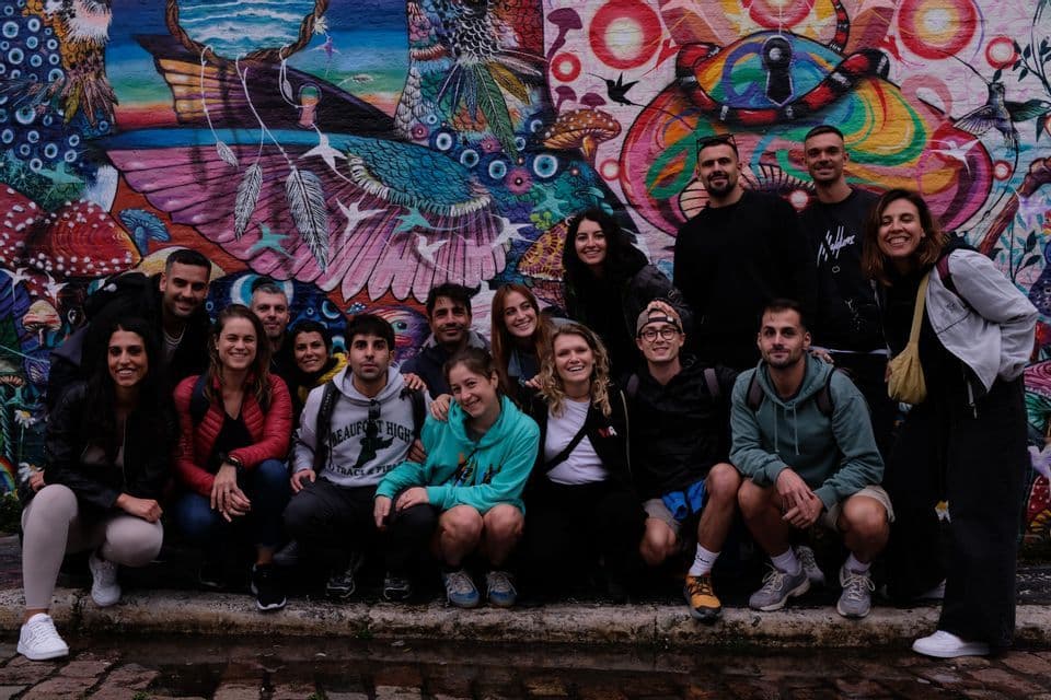 Un voyage de groupe WeRoad posant pour une photo de groupe devant une fresque de graffitis colorée et complexe dans une rue de ville.