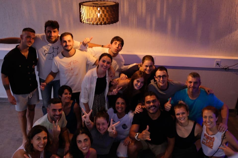Un voyage de groupe WeRoad avec des personnes souriantes posant ensemble pour une photo à l'intérieur, sous un luminaire moderne.