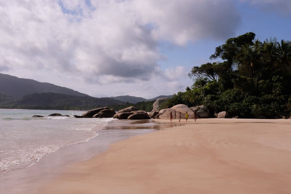 Un voyage en groupe WeRoad marchant le long d'une large plage de sable, à côté de grands rochers et d'une colline luxuriante couverte d'arbres.