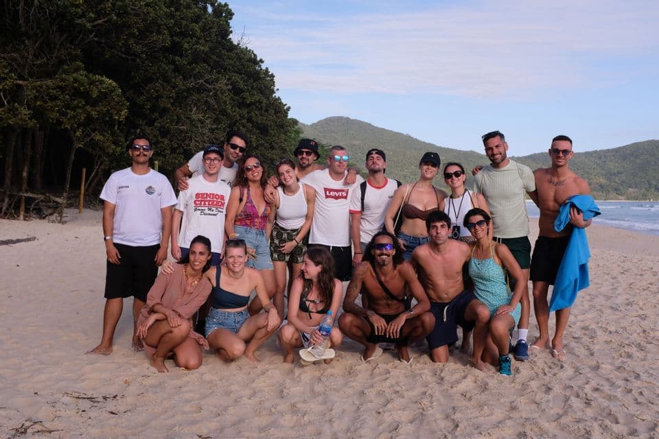 Un viaggio di gruppo WeRoad in posa per una foto su una spiaggia sabbiosa, con una foresta e colline sullo sfondo.