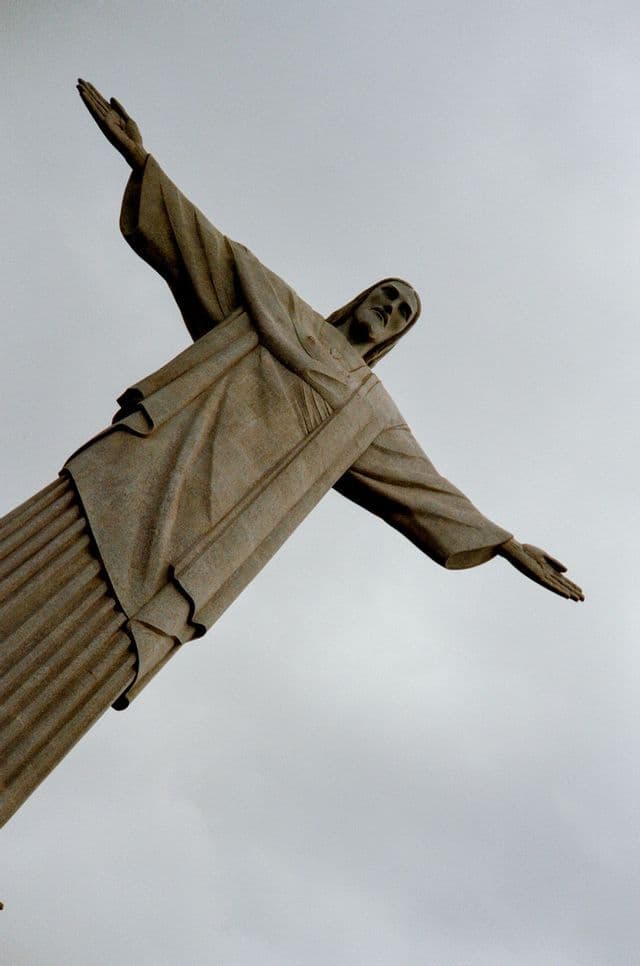 Un'inquadratura diagonale dal basso della statua del Cristo Redentore con le braccia aperte su un cielo coperto.